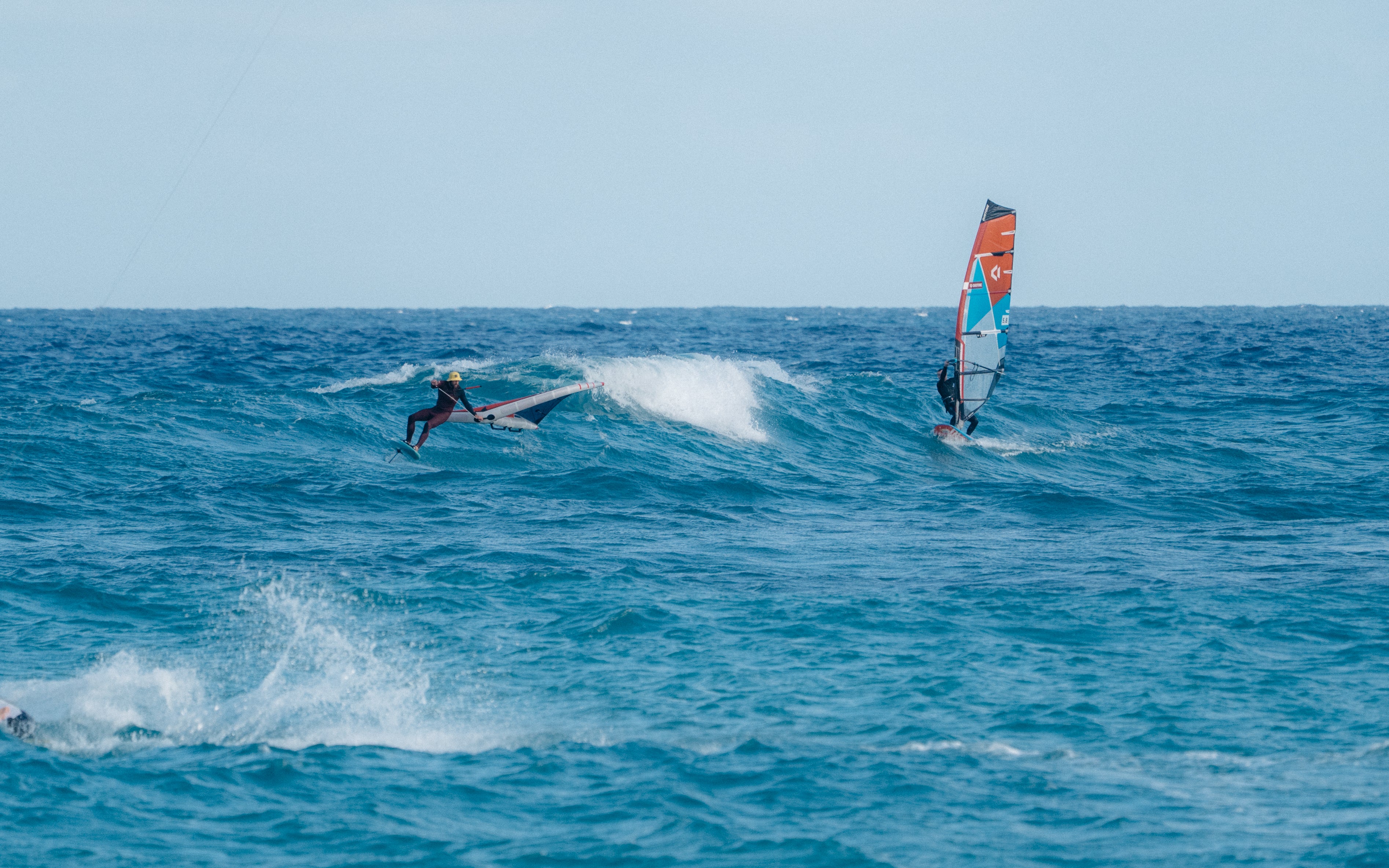 Rider en wing foil sur les vagues en mer aux côtés d'un planchiste à voile